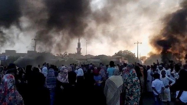 Mensen kijken naar rookpluimen die opstijgen van de Soedanese hoofdstad Khartoem. In Soedan is maandag mogelijk een staatsgreep gaande.