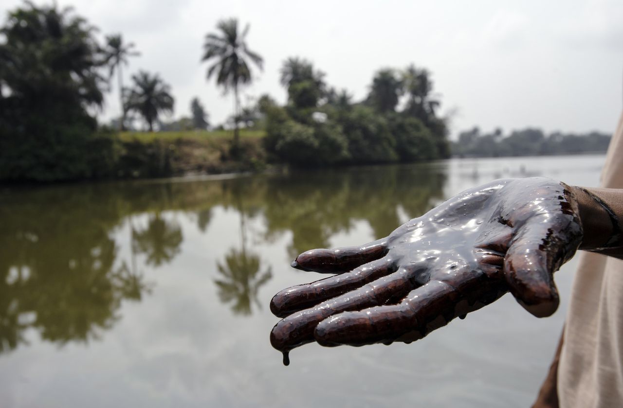 Een inwoner van Goi (Ogoniland, Nigeria) toont zijn hand die besmeurd is met ruwe olie, die de oevers van de kreek door het dorp heeft aangetast.