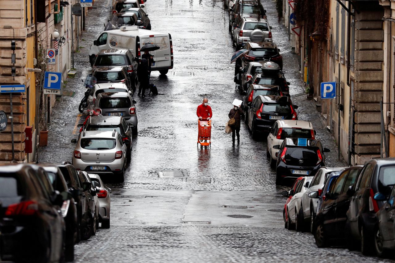 Een man met mondmasker loopt met een winkelwagentje over straat in Rome. De Italiaanse economie wordt volgens het IMF het zwaarst getroffen door de coronacrisis.