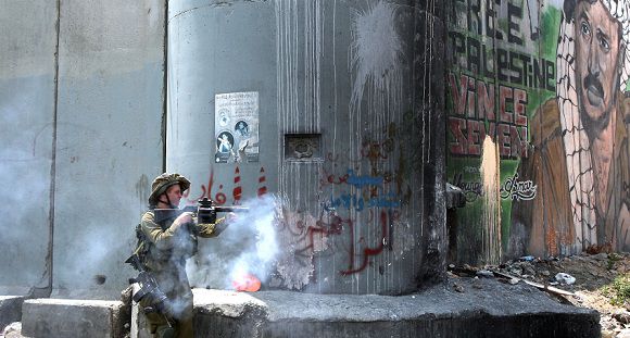 Caption: An Israeli soldier fires a stun grenade at Palestinian protesters in front of a section of Israel?s controversial "separation barrier", at Qalandia close to the West Bank city of Ramallah on July 9, 2011, on the seventh anniversary of a ruling by the International Court of Justice in The Hague that termed illegal Israel's construction of the 720-km (430-mile) barrier in the Israeli occupied West Bank. AFP PHOTO/ABBAS MOMANI