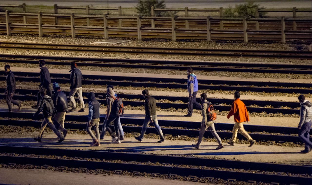Illegale vluchtelingen lopen over het spoor nabij de Franse terminal van de Eurotunnel, die treinen onder het kanaal door tussen Frankrijk en Groot-Brittannië vervoert.