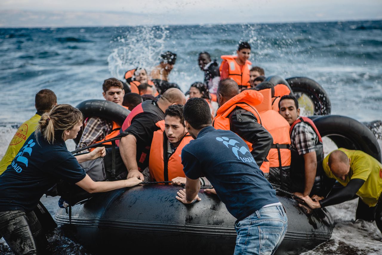 Vrijwilligers helpen migranten aan boord van de rubberboot waarmee ze op 30 september 2015 op het Griekse eiland Lesbos zijn aangekomen.