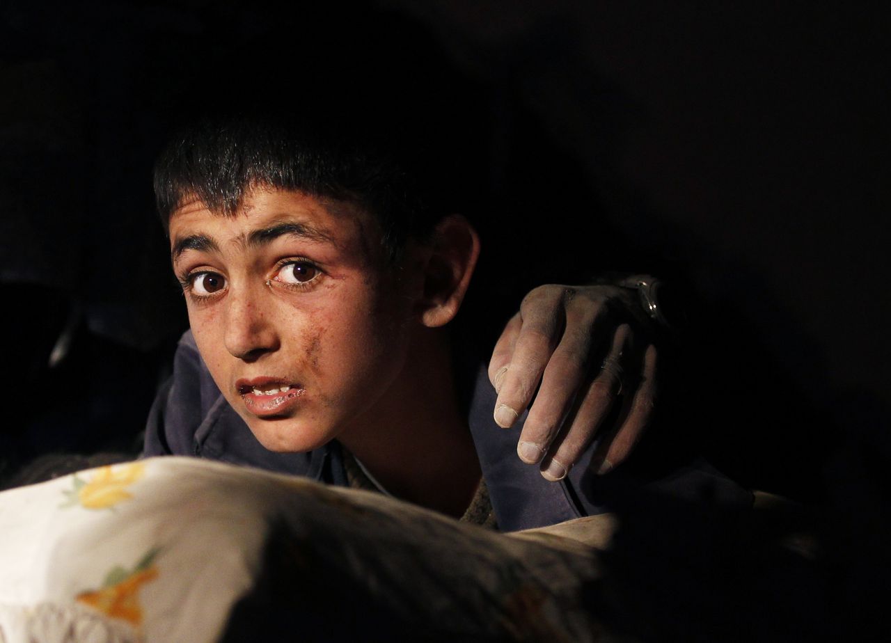 Yunus, a 13-year-old earthquake survivor with a hand of a victim on his shoulder, waits to be rescued from under a collapsed building by rescue workers in Ercis, near the eastern Turkish city of Van, early October 24, 2011. More than 100 people were confirmed killed and hundreds more feared dead on Sunday when a powerful earthquake hit southeast Turkey, flattening buildings and leaving survivors crying for help from under the rubble. REUTERS/Umit Bektas (TURKEY - Tags: DISASTER ENVIRONMENT TPX IMAGES OF THE DAY)