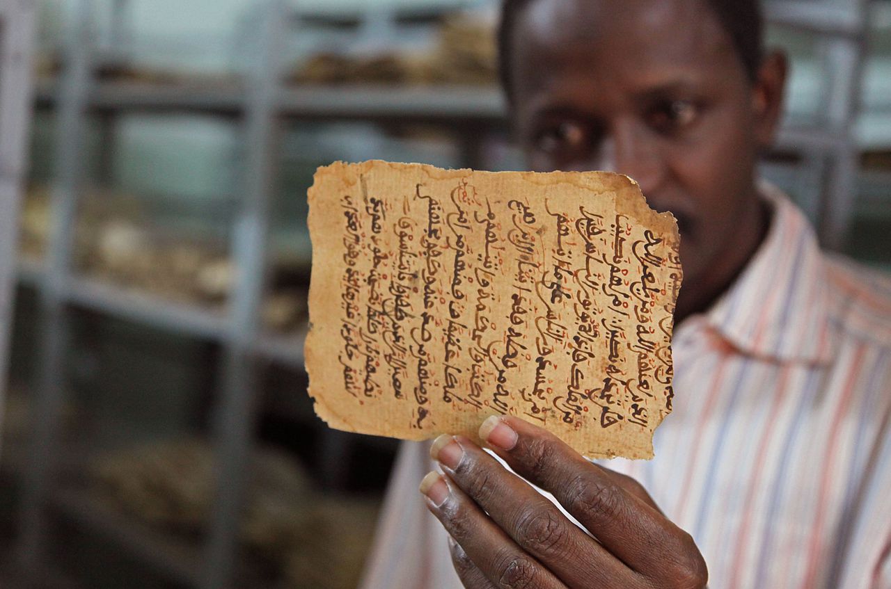 Een man in Bamako houdt een pagina van een oud manuscript in zijn handen dat is beschadigd.