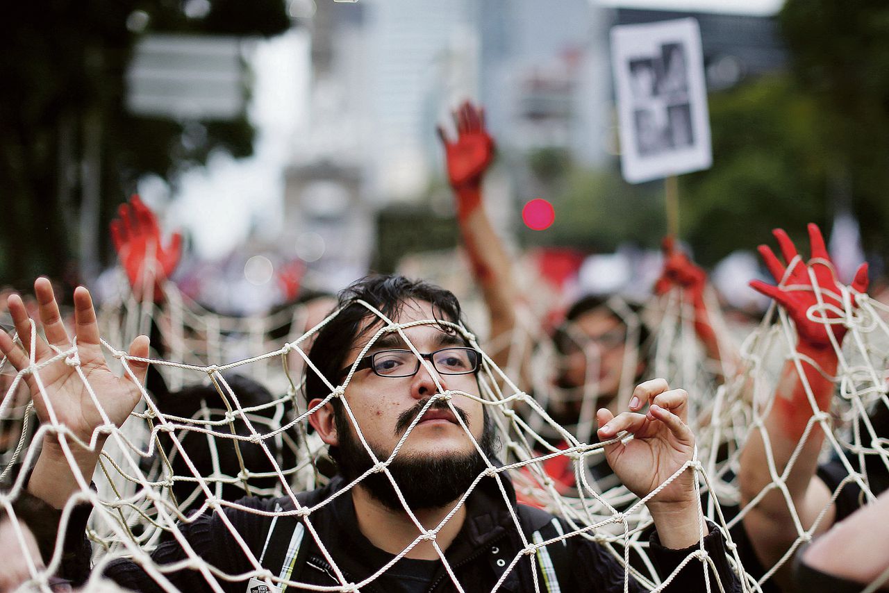 Betogers steken hun veelal roodgeverfde handen door een net, gisteren in Mexico-Stad. Zij eisten opheldering over het lot van 43 verdwenen studenten.