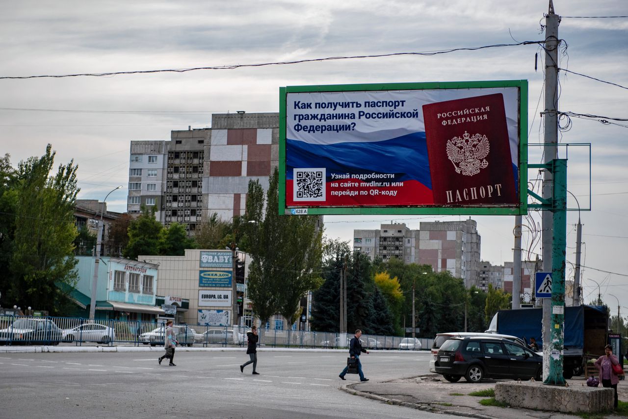 Mensen steken een straat over bij een reclamebord met de tekst "Hoe krijg ik een Russisch paspoort?", voorafgaand aan het schijnreferendum in de bezette regio Loehansk.