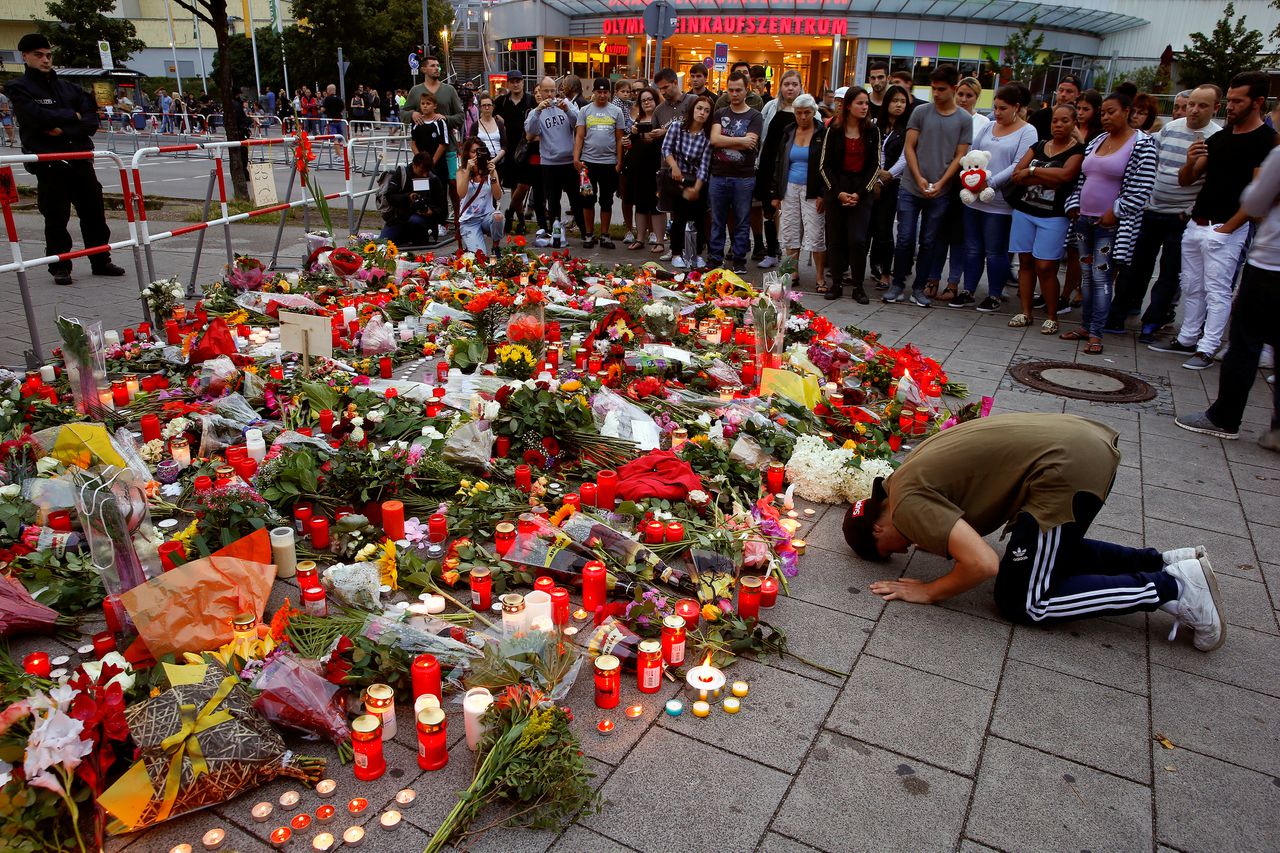 Een man bidt bij de bloemenzee die is ontstaan op de plek van de schietpartij in München.