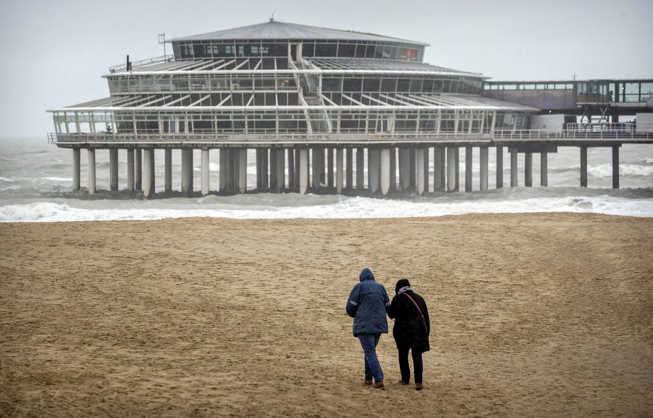 Wandelaars trotseren zondag de harde wind op het strand van Scheveningen.