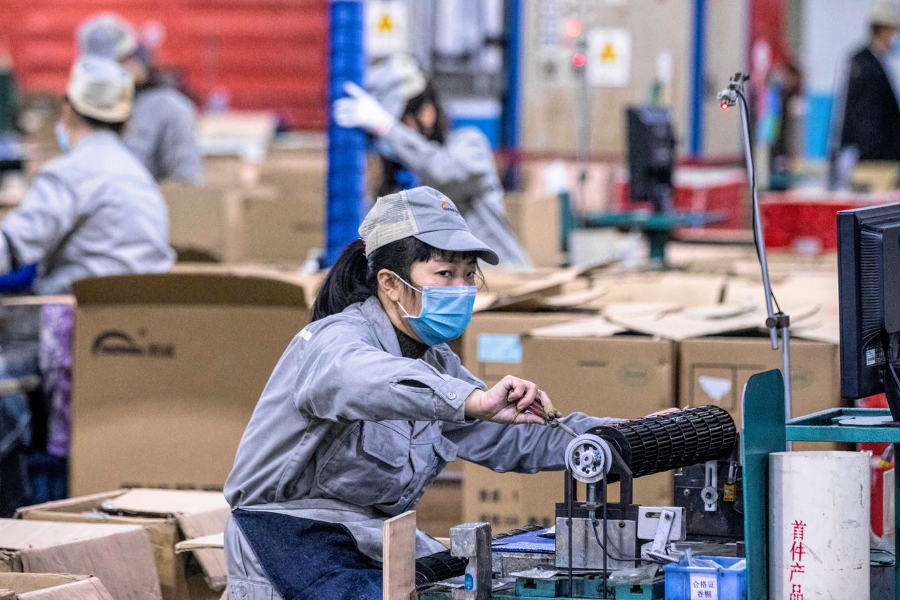 Een vrouw met een mondkapje in een Chinese fabriek. In veel Chinese steden zijn fabrieken stilgelegd om het coronavirus.