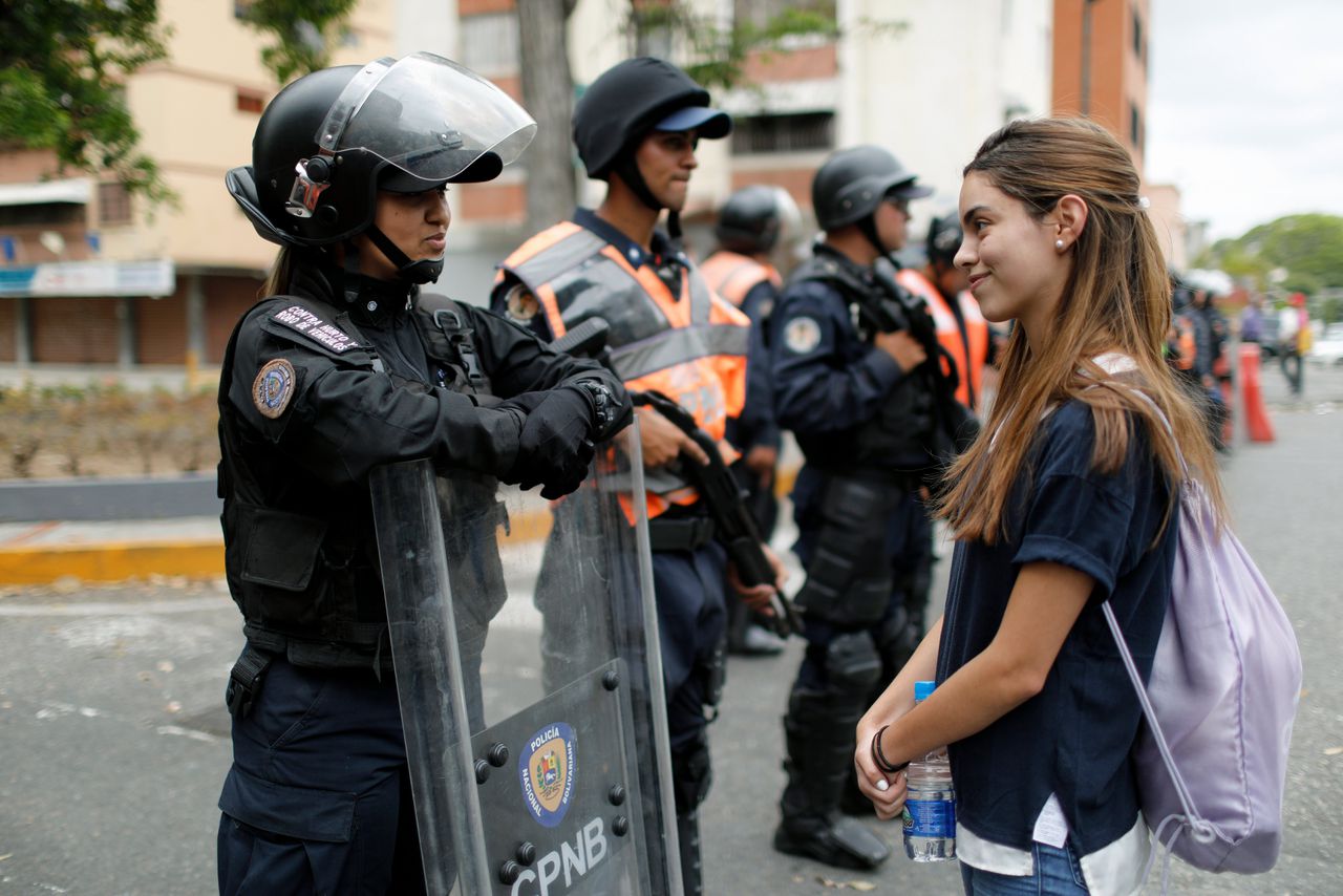 Een aanhanger van Guaidó staat glimlachend voor een agent van de oproeppolitie tijdens een protestmars zaterdag.