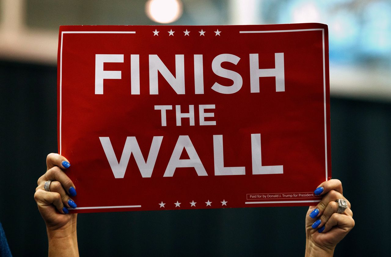 Een aanhanger van Donald Trump houdt een poster in de lucht waarop staat: 'maak de muur af', verwijzend naar de muur de Donald Trump wil laten bouwen op de grens met Mexico.