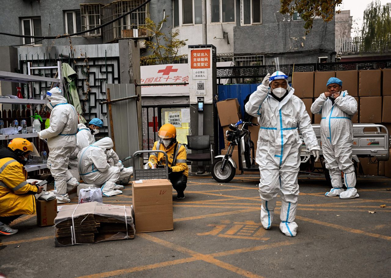 Gezondheidsmedewerkers bewaken de ingang van een woonwijk in Beijing waar een strenge lockdown geldt vanwege het coronavirus.