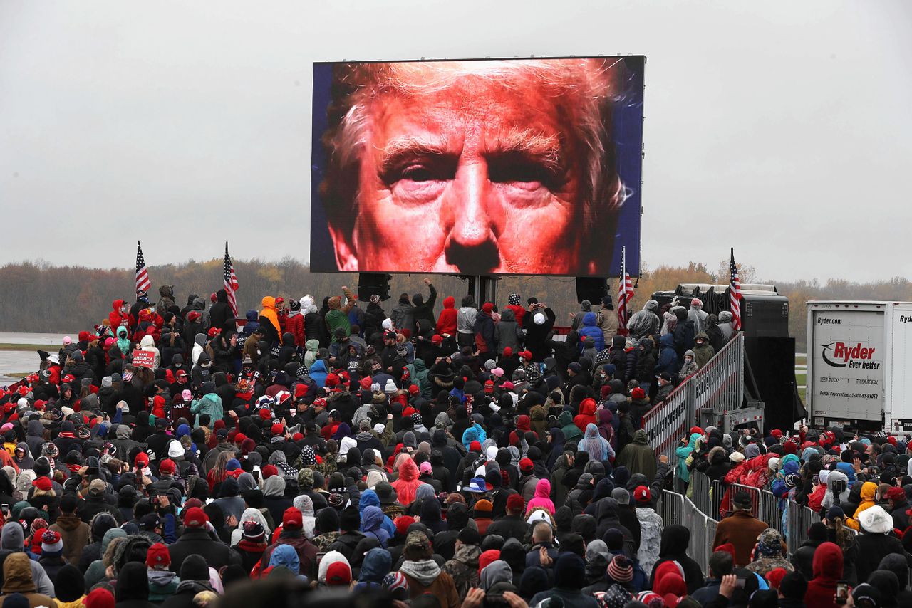 Fans bekijken een video van Donald Trump op een groot scherm in Lansing, Michigan.