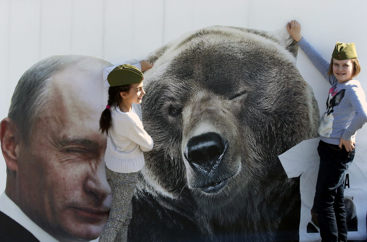 Russische kinderen poseren bij een affiche van Poetin naast een beer in de buurt van het park der overwinning in Moskou.