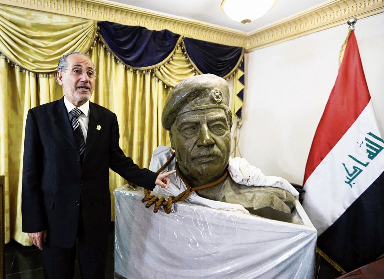 Parlementslid Mowaffak al-Rubaie in zijn eigen woonkamer waar om de nek van het beeld van Saddam Hussein het touw van de galg hangt.