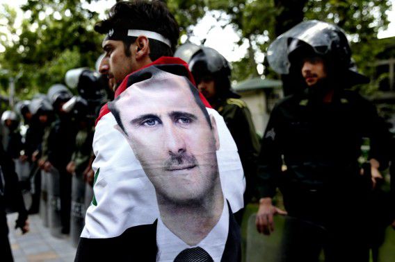 Een man met de Syrische vlag en beeltenis van Assad om zijn schouders loopt voorbij tijdens een demonstratie voor de deur van een VN-kantoor in Teheran, Iran.