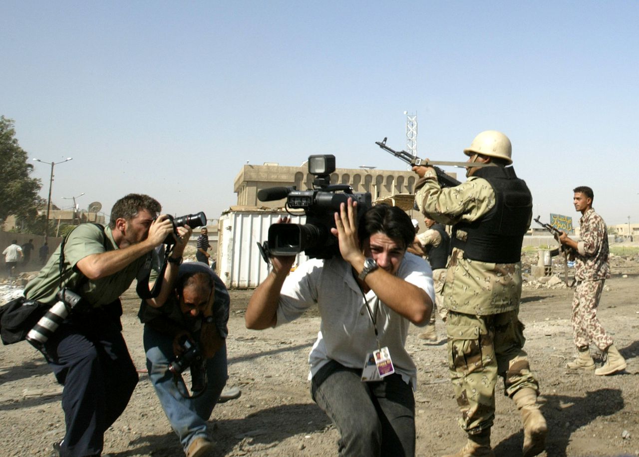 Een persfotograaf aan het werk in Bagdad. Strookt het beeld dat wij van Irak te zien krijgen wel met de werkelijkheid? Foto AFP A press photographer takes a picture as others run for cover while Iraqi security forces fire rounds in the air to disperse protestors who were chanting pro-Saddam Hussein slogans at the site of a suicide car bomb attack near a police station in southern Baghdad 19 July 2004. At least nine people were killed and 60 wounded. AFP PHOTO/Saeed KHAN