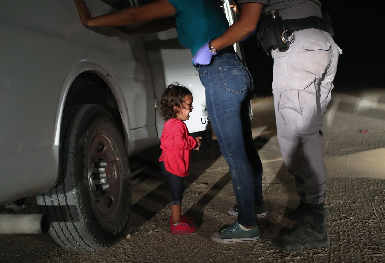 Een tweejarig kind uit Honduras huilt terwijl haar moeder gefouilleerd en gearresteerd wordt bij de grens met Mexico.