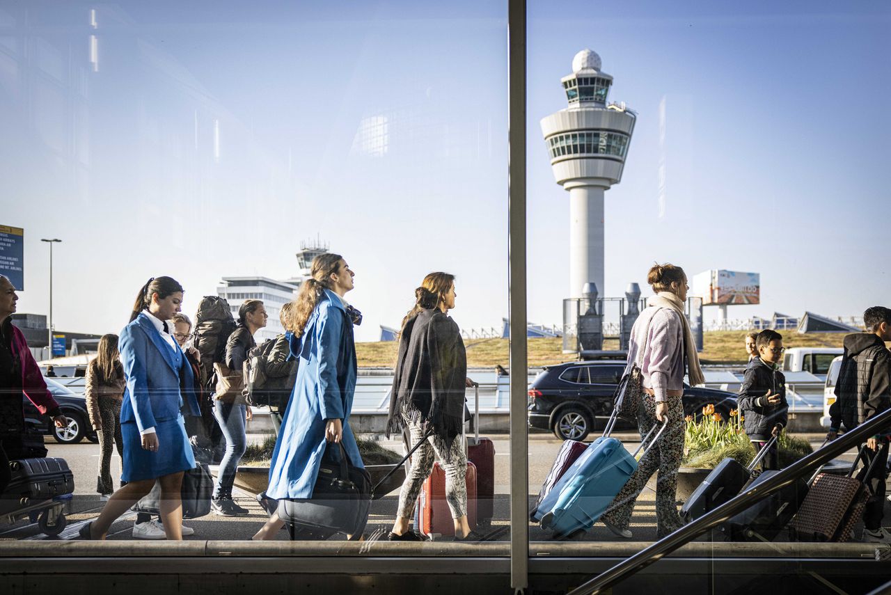 Reizigers staan buiten in de rij voor een vertrekhal op Schiphol.