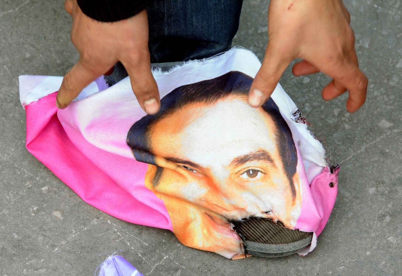 Een Tunesiër doet bij een demonstratie een stuk stof met de afbeelding van de afgezette Tunesische president Ben Ali om zijn schoen.