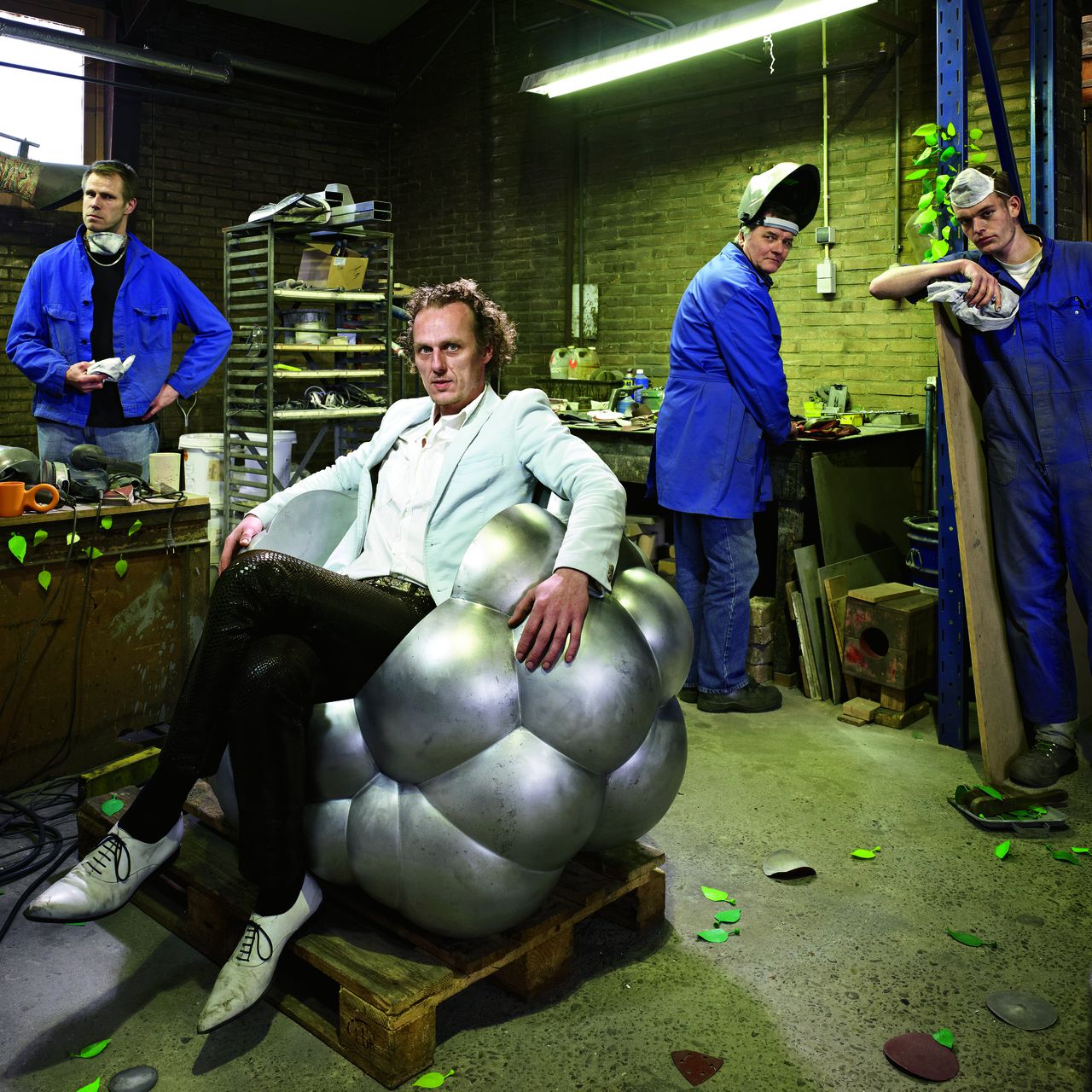 Richard Hutten zittend op een nog ongepolijst exemplaar van zijn jongste ontwerp, de aluminium Cloud Chair. Op de werkbank twee andere ontwerpen: zijn kinderbeker Domoor en de magnetische blaadjes Leaves.