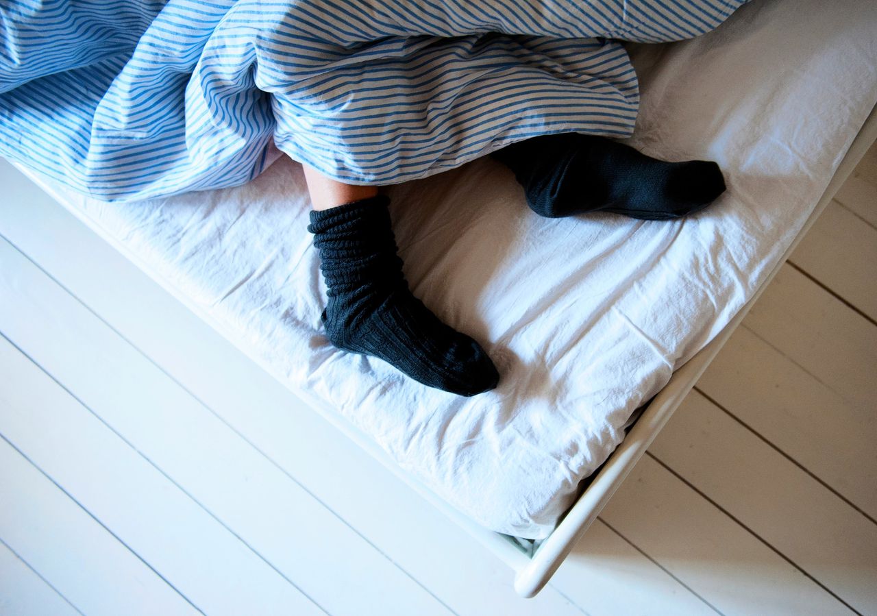 Een vrouw ligt met dikke sokken aan in bed. De erfelijke invloed op slapeloosheid is bij vrouwen groter dan bij mannen, vanwege de regeling van de hormoonhuishouding.