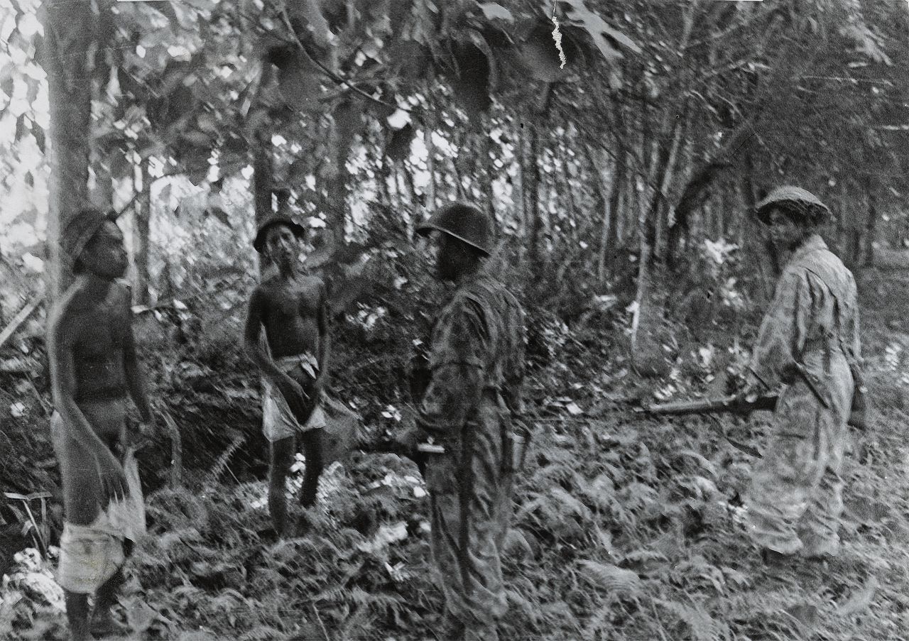 Twee KNIL-militairen houden op 22 juli 1947 in Bindjai (oostkust Sumatra) twee ontklede Indonesiërs onder schot. Het ontkleden van gevangenen kan men beschouwen als een vernedering waardoor zij nog kwetsbaarder tegenover de gewapende militairen stonden. Het oorspronkelijke bijschrift: “Iedereen die men tegenkomt die wordt ondervraagd, wat had dit eigenlijk voor nut?”