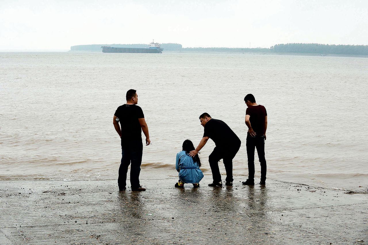 Een familielid van opvarenden van de Oostelijke Ster hurkt in wanhoop aan de oevers van de Yangtze.