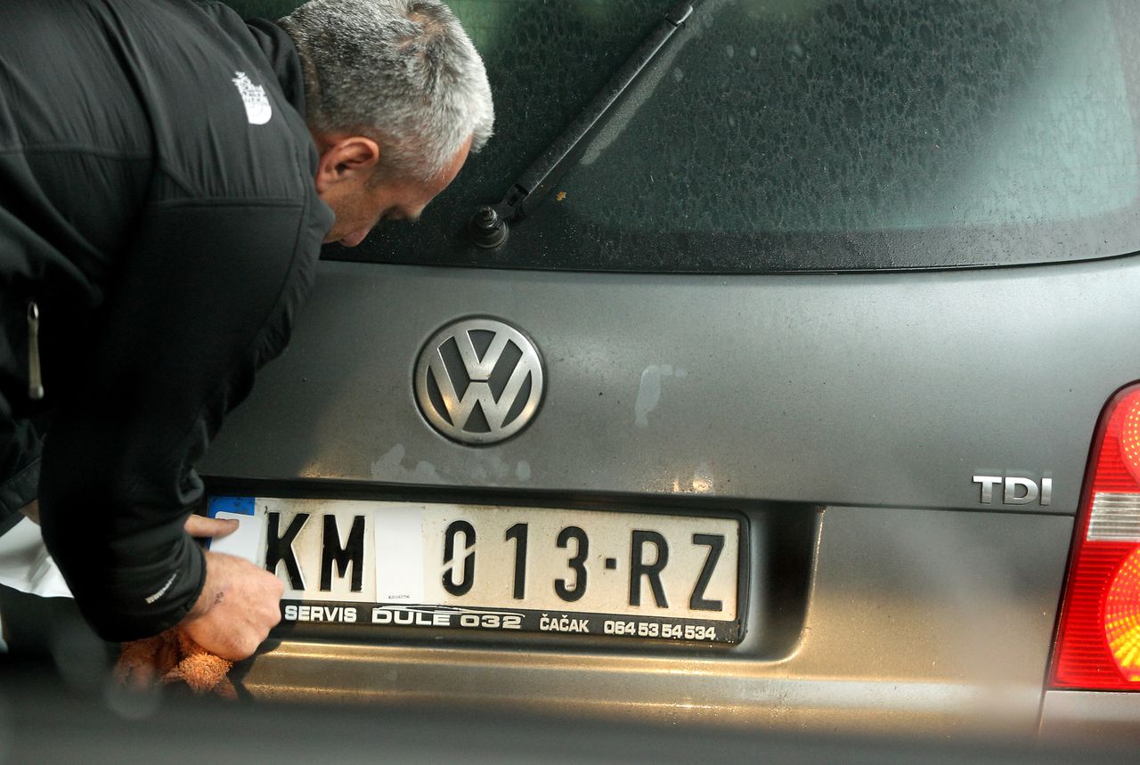 Een automobilist verwijdert stickers die de nationale markeringen op de kentekenplaten van zijn Servische auto bedekken.