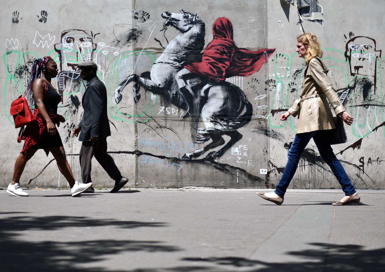 Een muurschildering in Parijs, vermoedelijk van de bekende artiest Banksy, toont Napoleon op een steigerend paard, verborgen onder rode doeken.