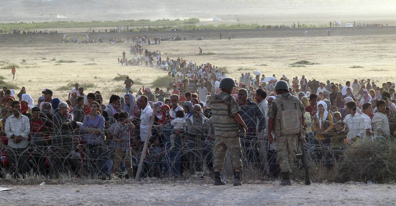 Turkse militairen staan op wacht terwijl aan de andere kant van de grens vluchtelingen uit de omgeving van Kobani zich verzamelen.