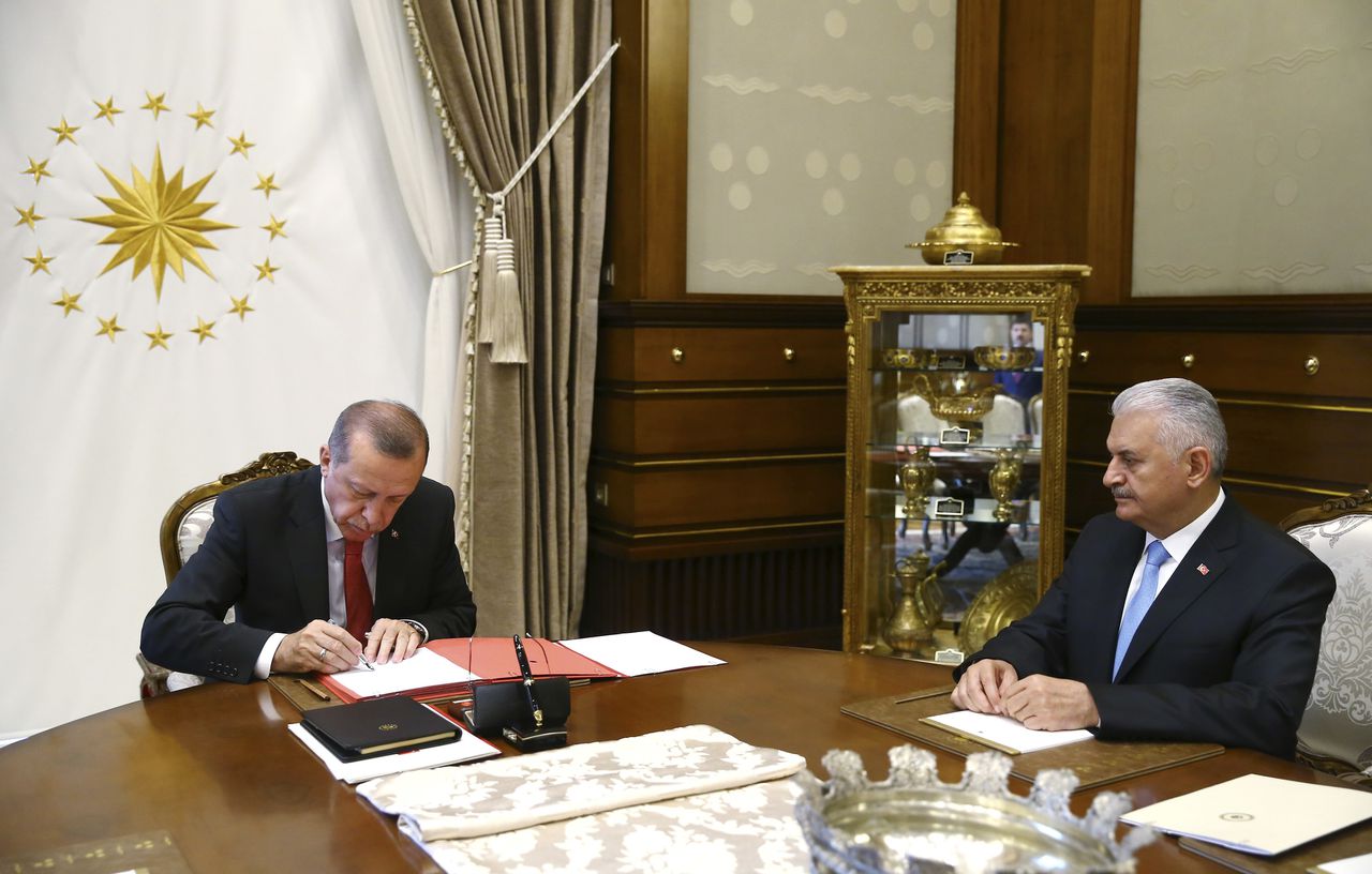 President Erdogan tekent het document waarin de herschikking van zijn kabinet is vastgesteld, terwijl premier Yildirim toekijkt.