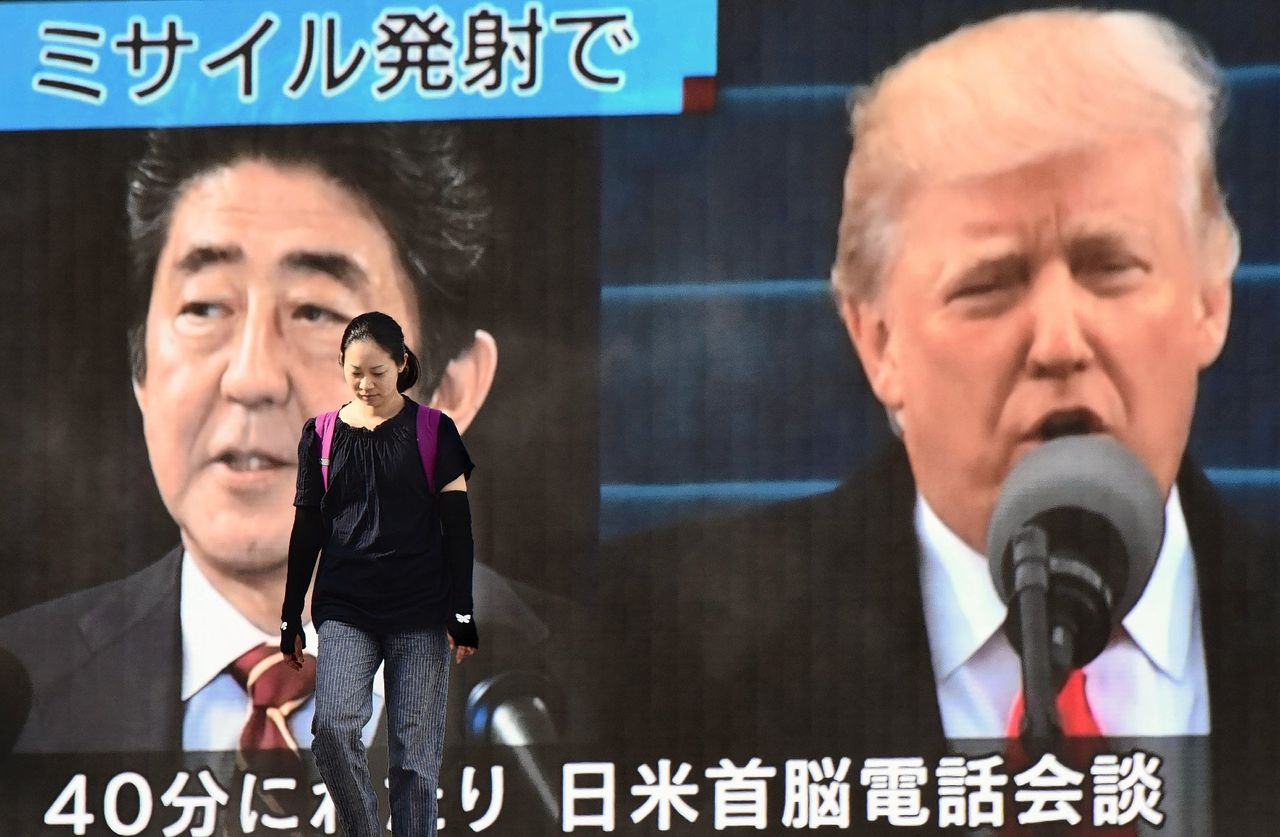 Een vrouw loopt langs een televisiescherm waarop de Japanse premier Abe en de Amerikaanse president Trump te zien zijn, nadat een Noord-Koreaanse raket eerder op de dag over Japan werd afgeschoten.