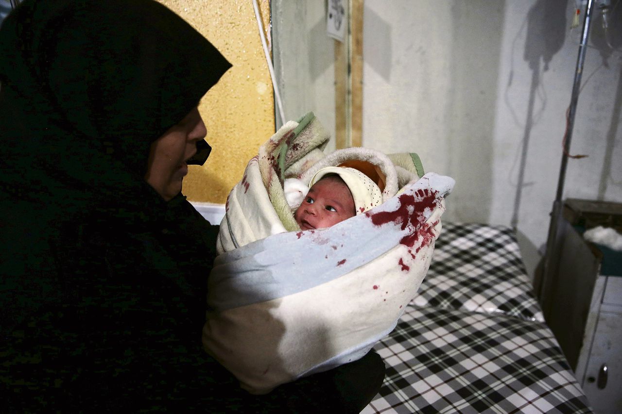 Een vrouw draagt een gewonde baby naar een veldhospitaal na een bombardement in een buitenwijk van Damascus.