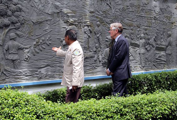 Ambassadeur Tjeerd de Zwaan kijkt naar een reliëf waarop de ramp waaraan Nederlandse militairen schuldig zijn wordt afgebeeld.