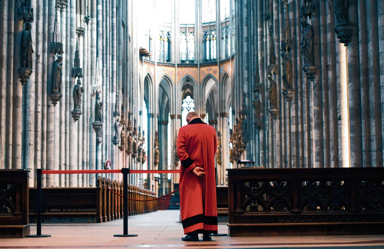 Een kerkelijke functionaris in een lege Dom van Keulen. Alle kerken en moskeeën zijn gesloten voor het publiek.
