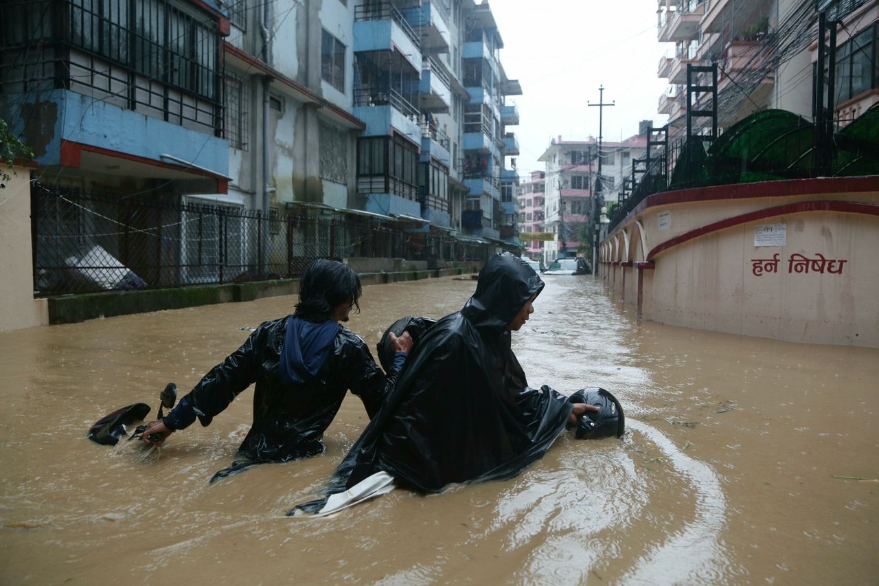 Nepalezen trekken hun motorfietsen door de overstroomde straten van hoofdstad Kathmandu.