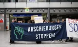  ·Stop deportations· reads a banner held by participants in a vigil at the terminal at Leipzig/Halle Airport. They are protesting against a suspected deportation flight to Afghanistan. Photo: Hendrik Schmidt/dpa