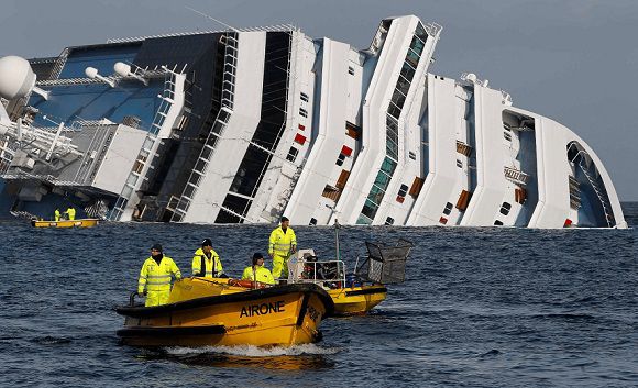 Caption: Oil recovery workers pass in front of the Costa Concordia cruise ship which ran aground off the west coast of Italy at Giglio island and is now half-submerged and threatening to slide into deeper waters January 22, 2012. A week after the 114,500-tonne ship ran aground and capsized off the Tuscan coast, hopes of finding anyone alive have all but disappeared. Diving crews recovered the body of a woman aboard the ship on Saturday, bringing the death toll to at least 12. Twenty people are unaccounted for and hopes of finding anyone alive have all but gone. REUTERS/Paul Hanna (ITALY - Tags: DISASTER TRANSPORT TPX IMAGES OF THE DAY)