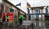 Een Greenpeace-activist fietst langs de Duitse kanselarij in Berlijn met een poster waarop bondskanselier Olaf Scholz staat afgebeeld met de tekst: ‘Kanselier voor verbrandingsmotoren’ (in plaats van klimaatbescherming).