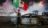 A demonstrant waves on Saturday with a Mexican flag at a burned out car wreck full of graffiti directed against the federal immigration police. Photo Ringo Chiu/AFP)  