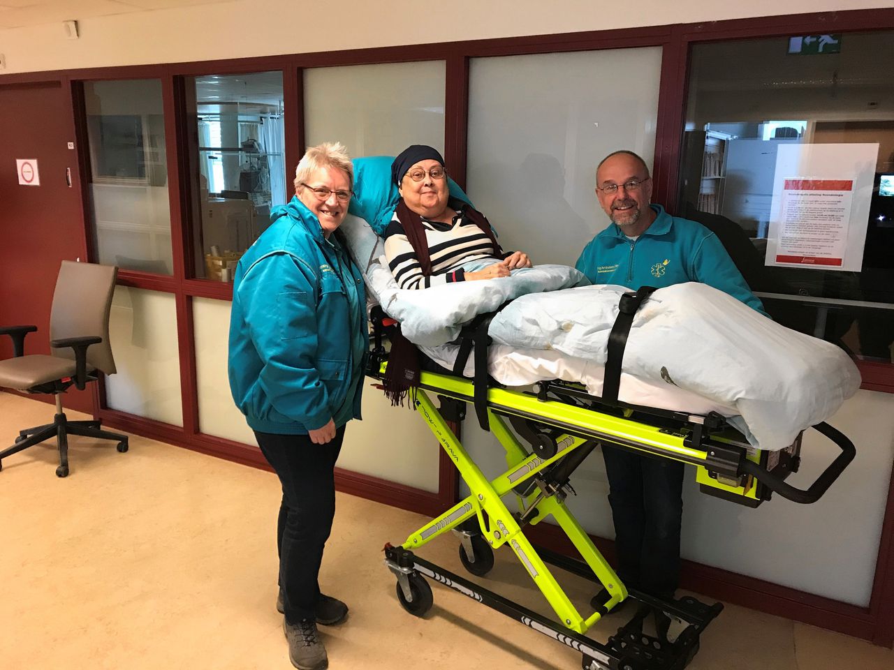 Margot Lee in het ziekenhuis voor een bezoek aan haar pasgeboren kleinkind, met twee medewerkers van stichting Ambulance Wens.