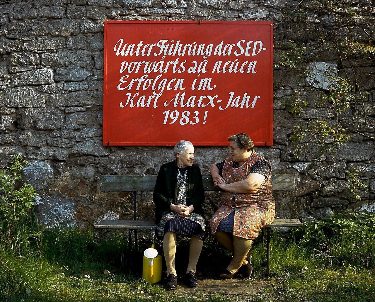 Twee oude vrouwen op een bankje in Thüringen, met achter hen een bord voor het Karl Marx-jaar (1983)