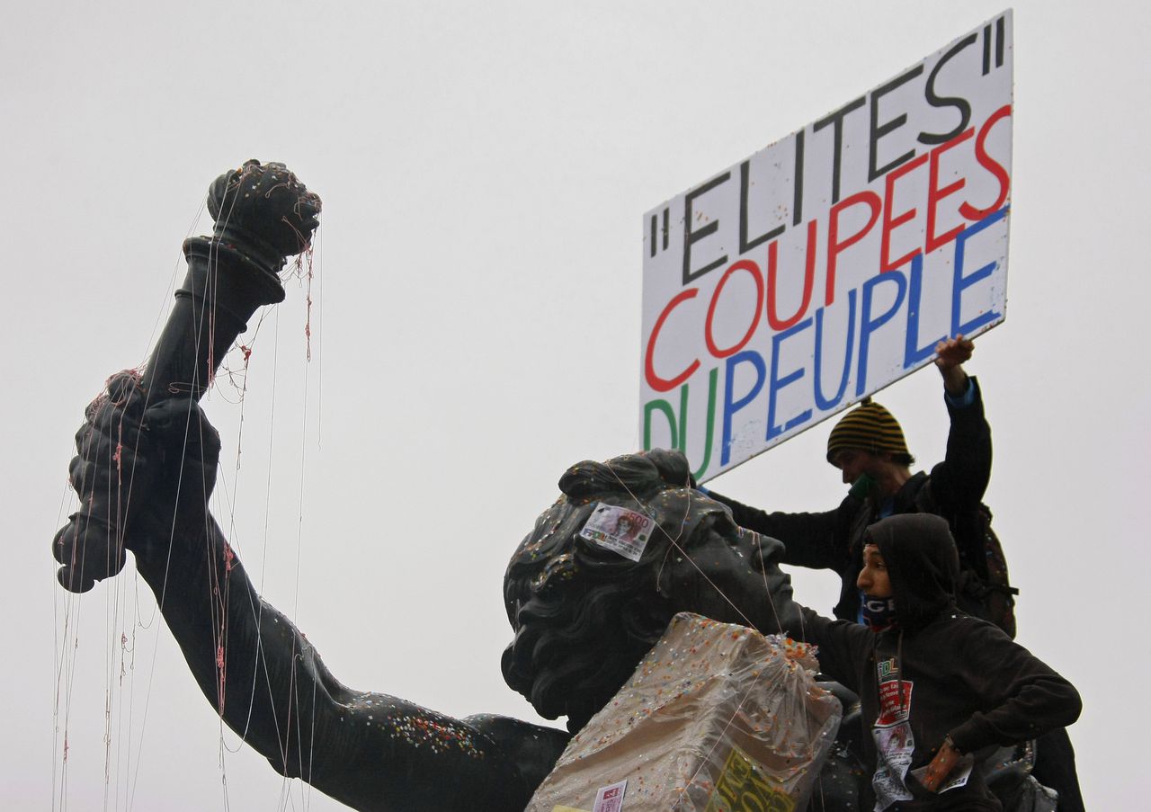 A demonstrator holds a placard which reads 'the elite is cut off from the people', as he stands on a statue during a rally to protest France's decision to raise the retirement age, in Paris, Saturday, Nov. 6, 2010.(AP Photo/Michel Spingler)