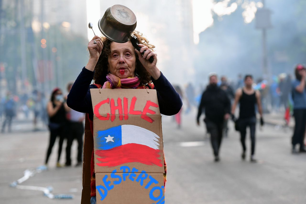 Een Chileense vrouw loopt slaande op een pan mee in een protestmars. Op het bord staat: ‘Chili is wakker geworden.