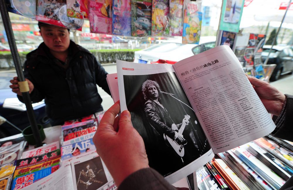 Een klant van een krantenkiosk in Beijing bekijkt een tijdschrift met een foto van Bob Dylan.