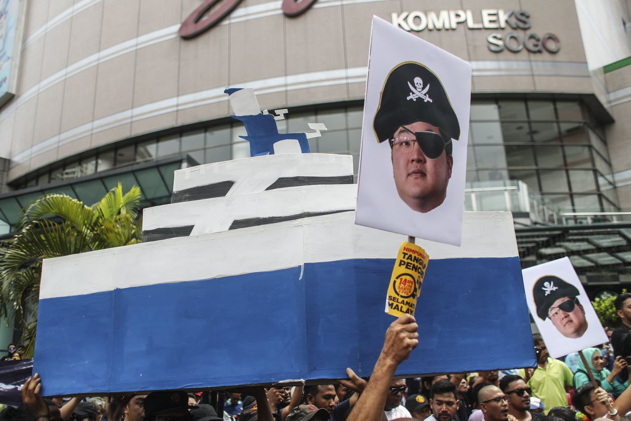 Demonstranten in de Maleisische hoofdstad Kuala Lumpur houden een bord omhoog met de afbeelding van Jho Low.