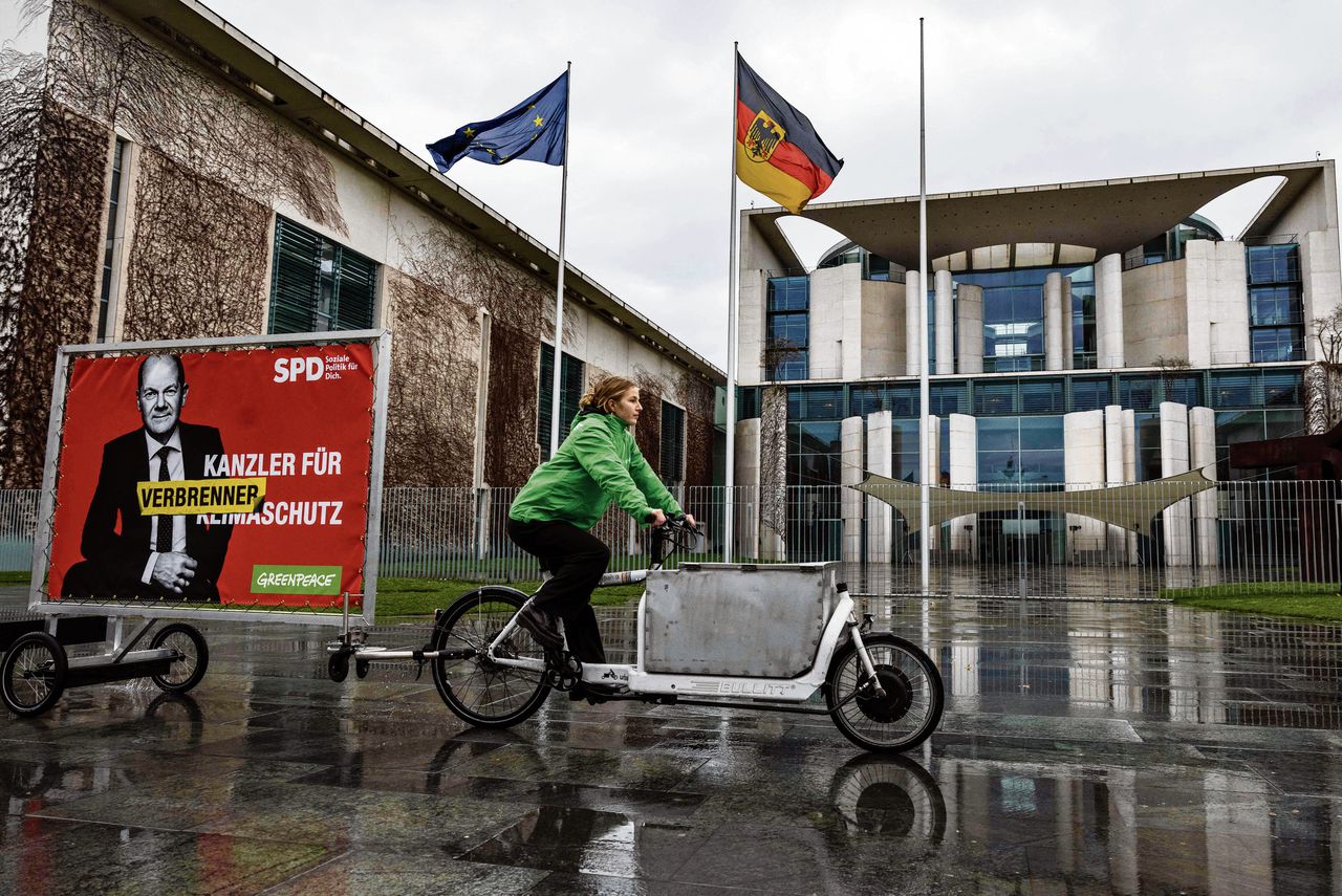 Een Greenpeace-activist fietst langs de Duitse kanselarij in Berlijn met een poster waarop bondskanselier Olaf Scholz staat afgebeeld met de tekst: ‘Kanselier voor verbrandingsmotoren’ (in plaats van klimaatbescherming).