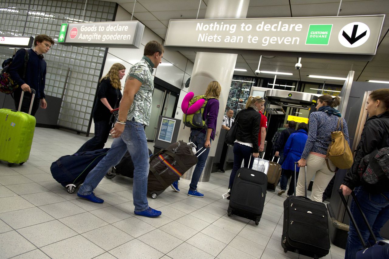 Teruggekeerde reiziger arriveren op de luchthaven Schiphol en moeten voor controle langs de douane.