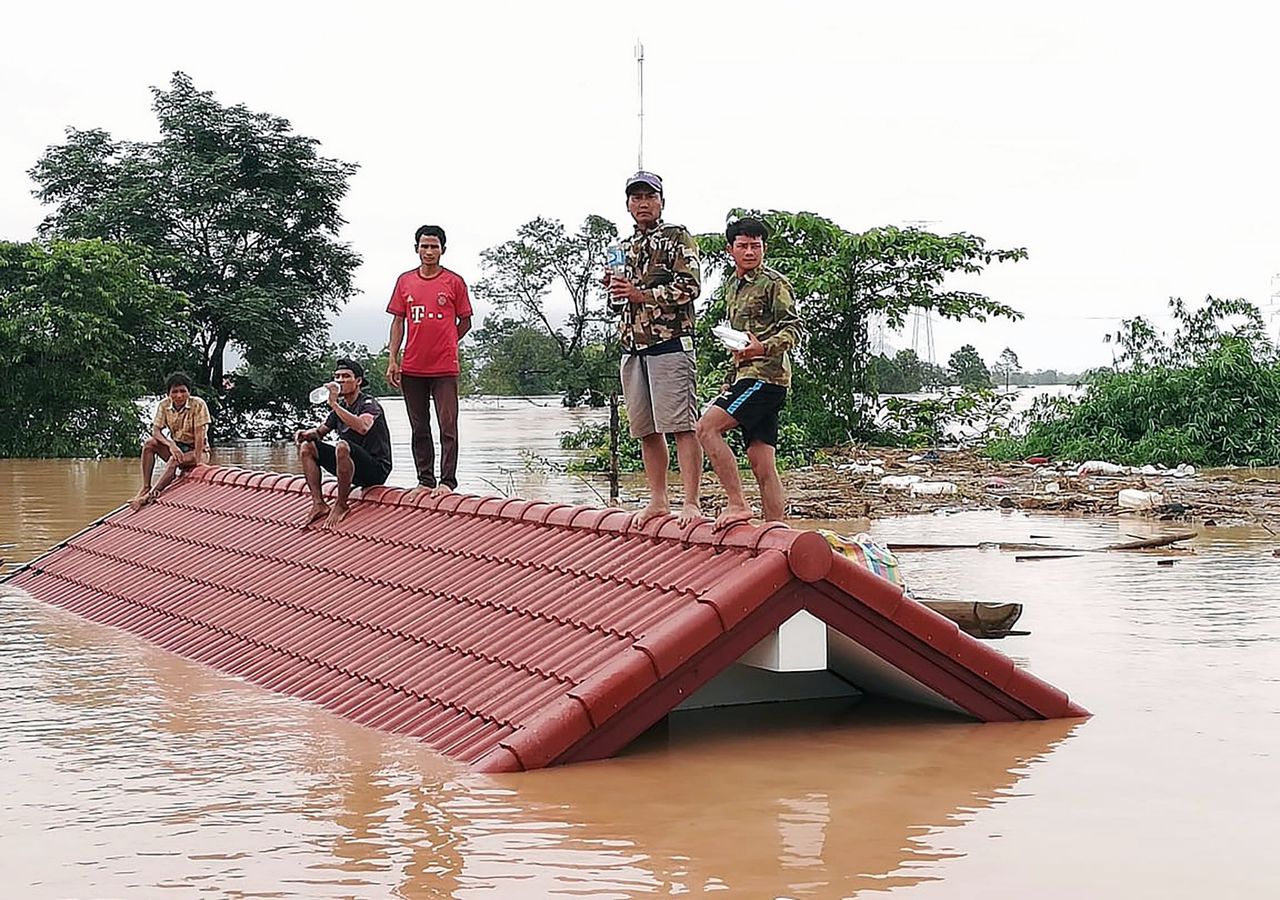 Laotianen zijn naar het dak van hun huis gevlucht, nadat het onder water is komen te staan door de dambreuk.